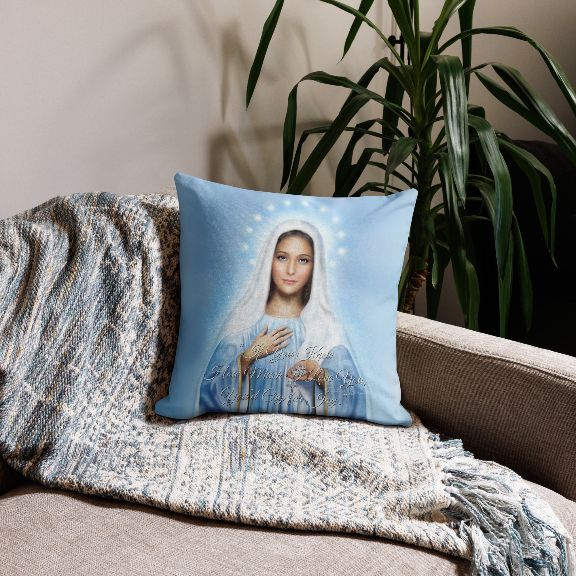 Photo of a pillow with the image of Our Lady of Medjugorje with words on it placed on a couch with a blanket